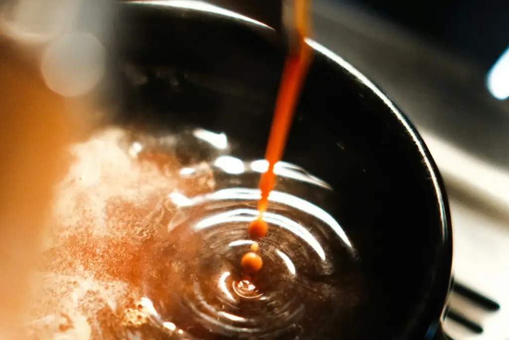 Espresso shot pouring into a dark cup, creating ripples