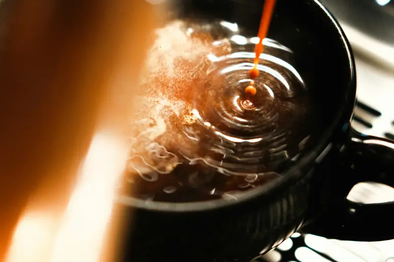 Espresso shot pouring into a dark cup, creating ripples