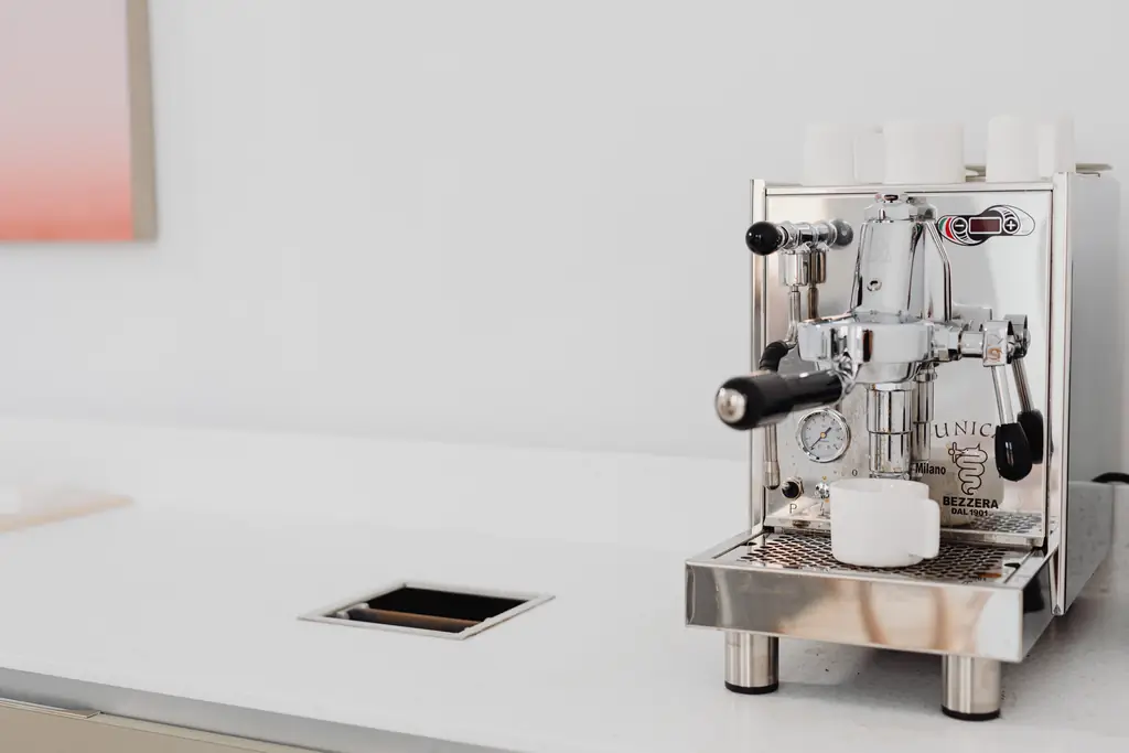 Stainless E61-style espresso machine with cups on top on a white counter