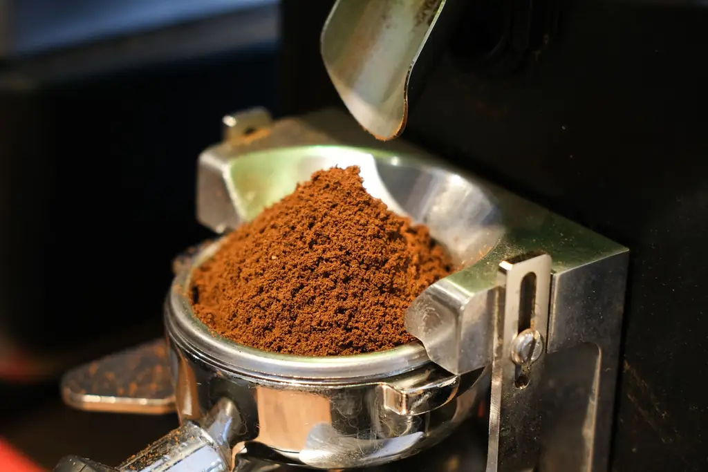 Espresso grinder dosing fresh grounds into a portafilter in its holder (illustrative)