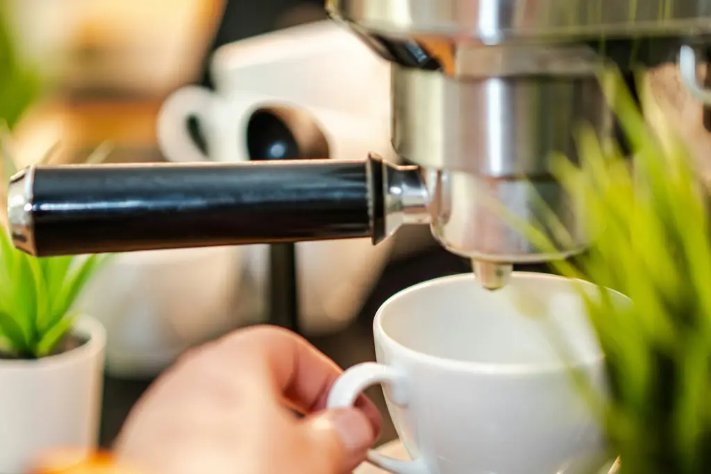 Hand holding a cup under a home espresso machine on a wooden counter