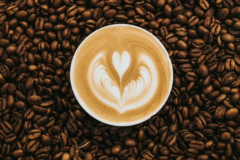 Heart latte art in a white cup surrounded by coffee beans