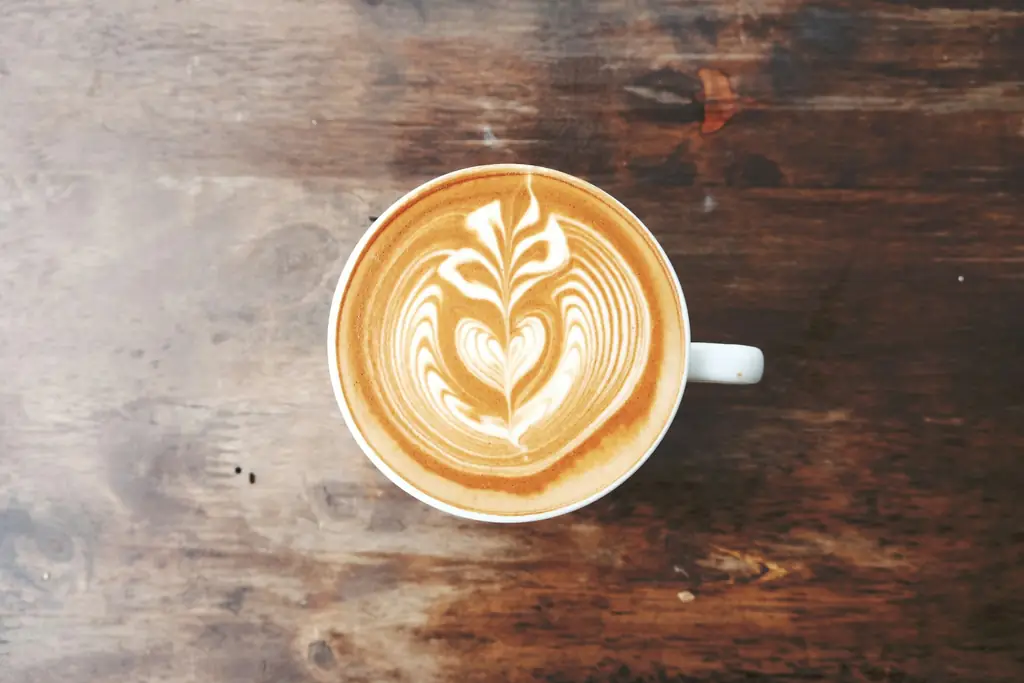 Latte art in a white mug on a dark wooden table, seen from above