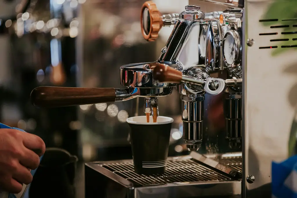 Chrome lever-style espresso machine pulling a shot into a cup