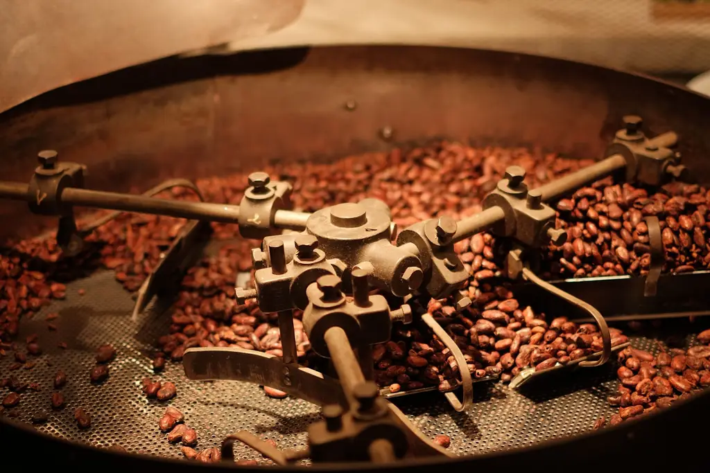 Roasted coffee beans turning in a roaster's cooling tray under warm light