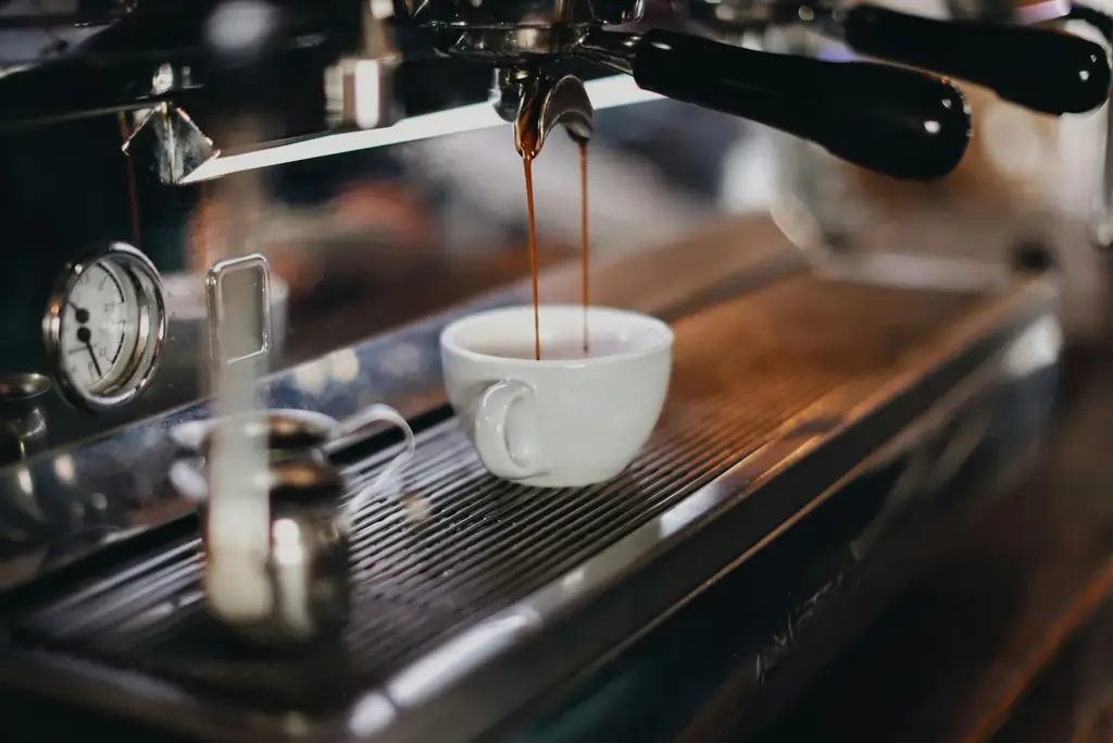 Espresso pouring from a machine's group head into a white cup