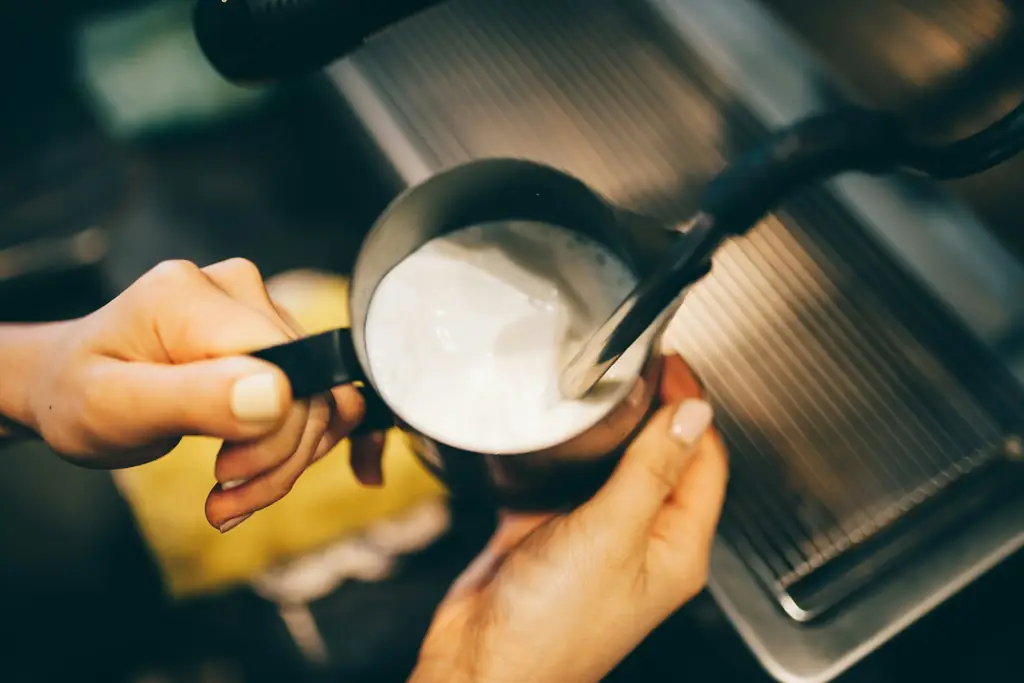 Hands steaming milk in a metal pitcher at an espresso machine